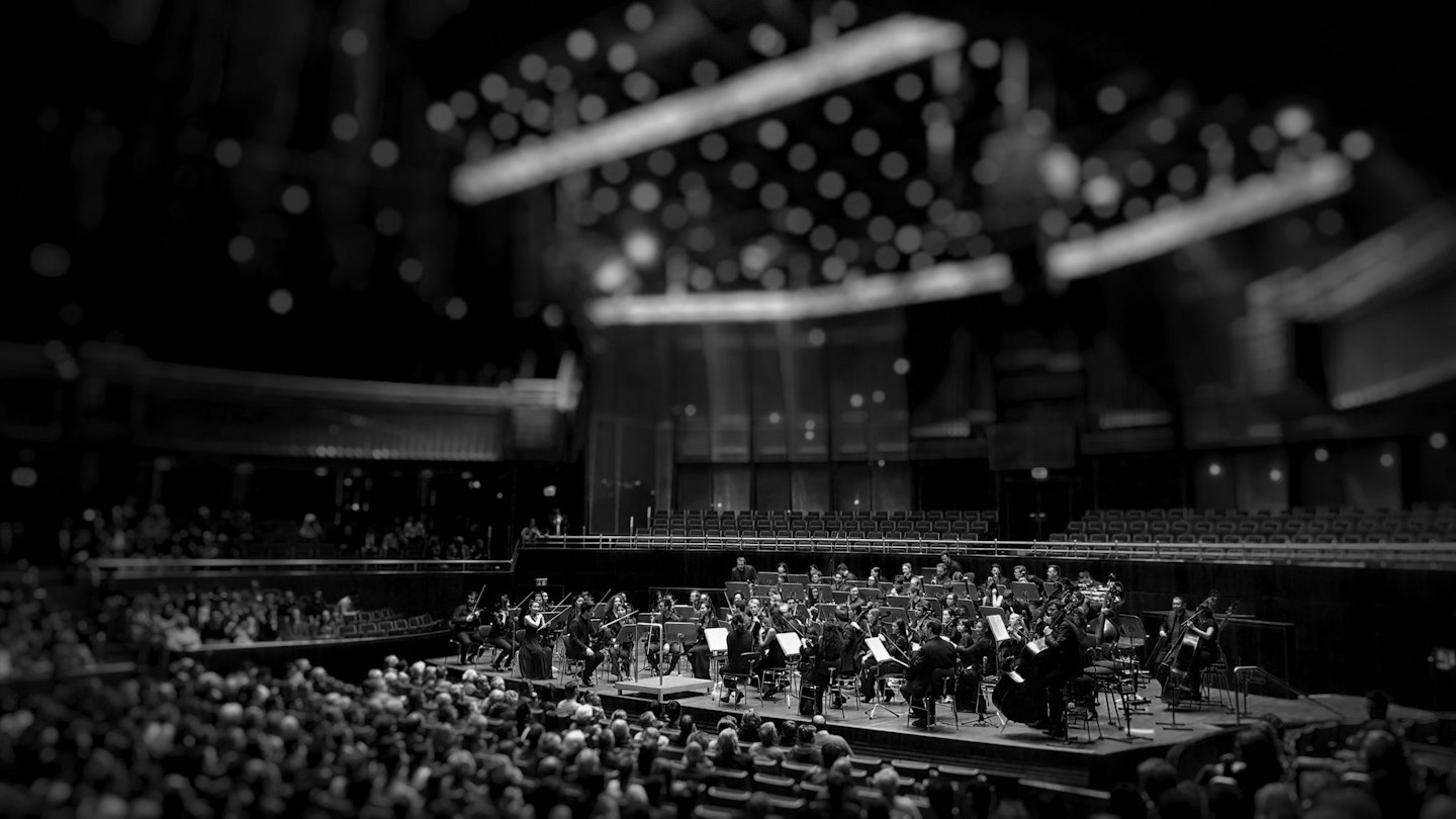 Symphony orchestra performing on a grand stage with a full audience.